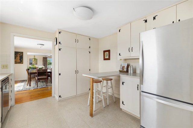 kitchen with white cabinetry, tasteful backsplash, light hardwood / wood-style flooring, a kitchen bar, and stainless steel appliances