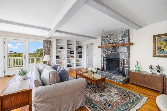 living room with light wood-type flooring, built in features, beam ceiling, and a stone fireplace