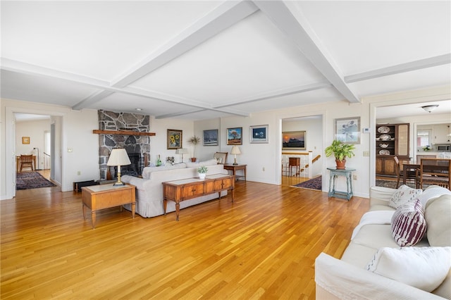 living room featuring hardwood / wood-style floors, beam ceiling, and a stone fireplace