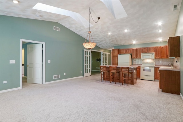 kitchen featuring light carpet, lofted ceiling with skylight, white appliances, a kitchen island, and decorative backsplash