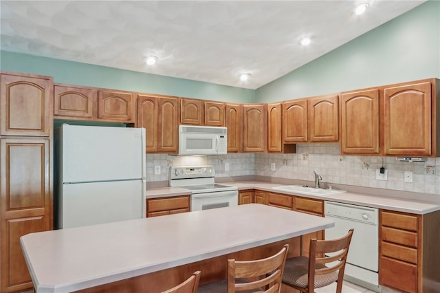 kitchen with vaulted ceiling, white appliances, a kitchen bar, sink, and decorative backsplash