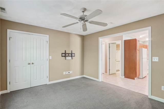 unfurnished bedroom featuring a closet, ceiling fan, light carpet, and white refrigerator