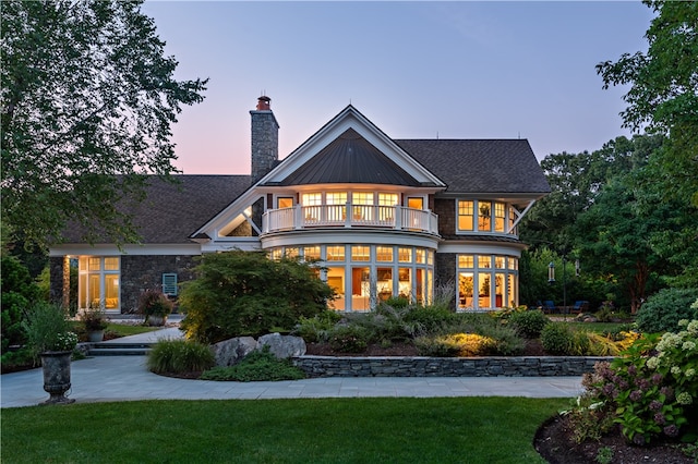 back house at dusk with a balcony and a lawn