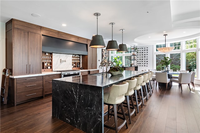 kitchen featuring a breakfast bar area, dark hardwood / wood-style floors, wall chimney exhaust hood, an island with sink, and dark stone counters