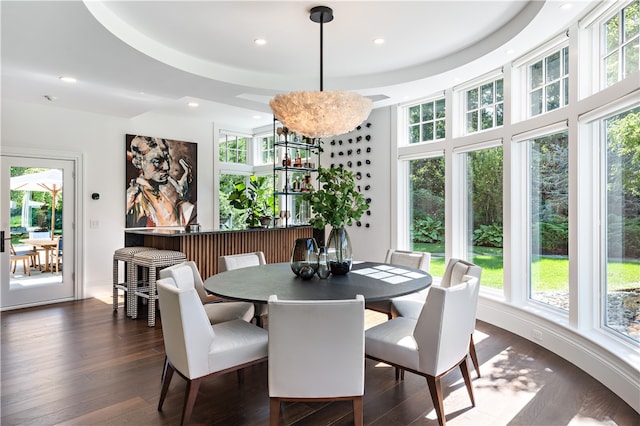 dining space with dark wood-type flooring, a raised ceiling, and a notable chandelier