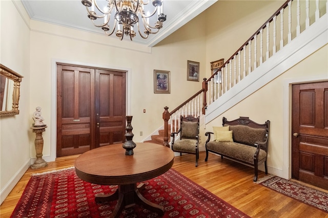 foyer with light wood-type flooring, a chandelier, crown molding, and a high ceiling