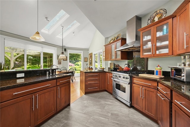 kitchen with wall chimney range hood, lofted ceiling with skylight, stainless steel range, sink, and hanging light fixtures