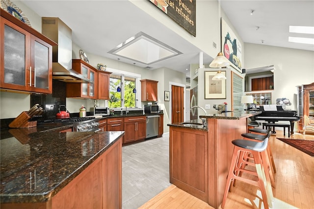 kitchen with stainless steel appliances, wall chimney exhaust hood, sink, light hardwood / wood-style floors, and hanging light fixtures