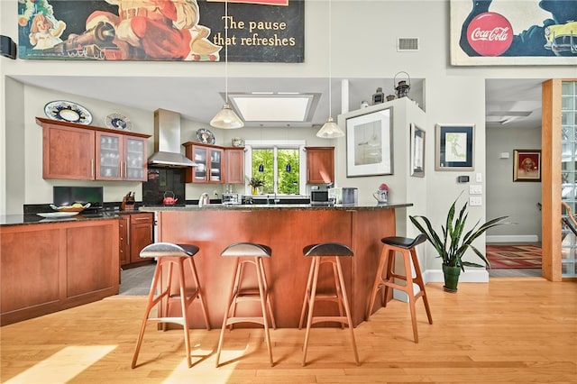 bar featuring wall chimney exhaust hood, dark stone counters, hanging light fixtures, and light wood-type flooring