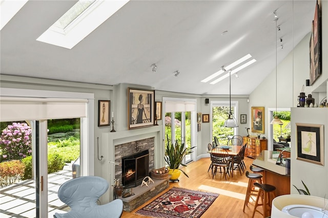 living room with a fireplace, high vaulted ceiling, light hardwood / wood-style flooring, and a skylight