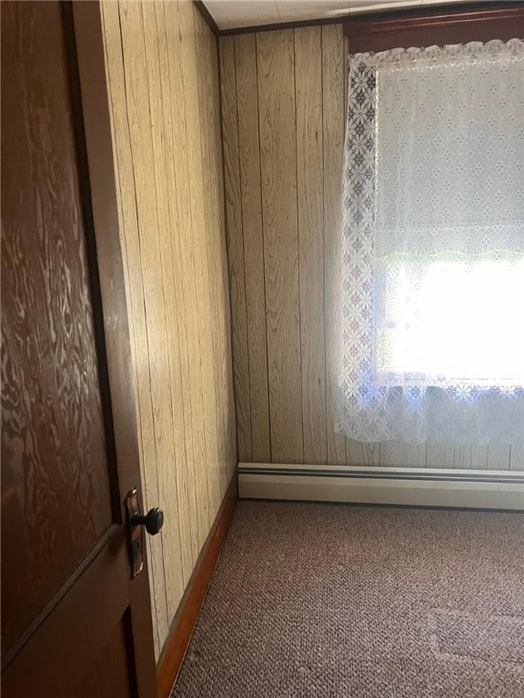 carpeted empty room featuring a baseboard radiator and wooden walls