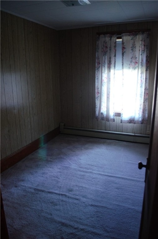 spare room with a baseboard heating unit, wooden walls, and carpet floors