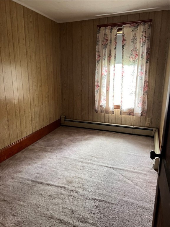 carpeted empty room featuring a baseboard radiator and wooden walls