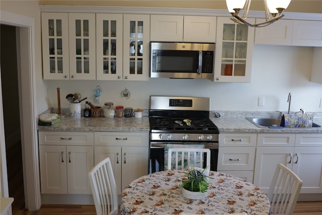 kitchen featuring appliances with stainless steel finishes, sink, a chandelier, light stone counters, and white cabinets