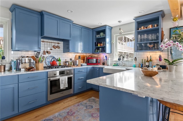 kitchen with light stone counters, light hardwood / wood-style floors, tasteful backsplash, a breakfast bar area, and appliances with stainless steel finishes