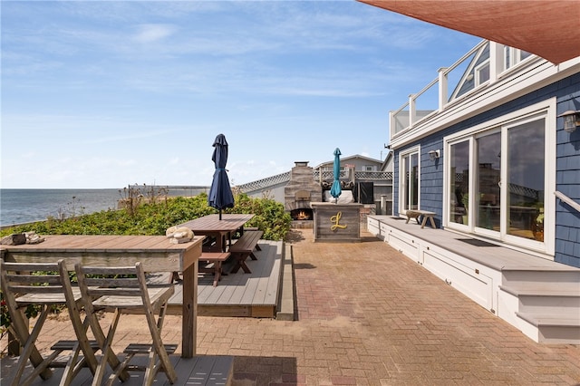 view of patio with an outdoor stone fireplace and a deck with water view