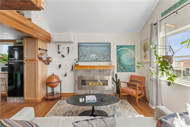 living room with a fireplace, vaulted ceiling, a wall mounted AC, and light hardwood / wood-style flooring