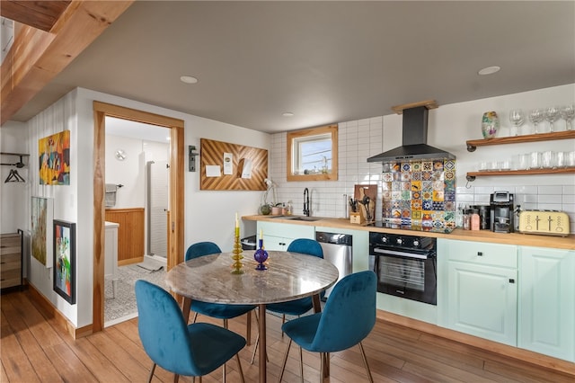 kitchen with sink, wall chimney exhaust hood, backsplash, oven, and light wood-type flooring