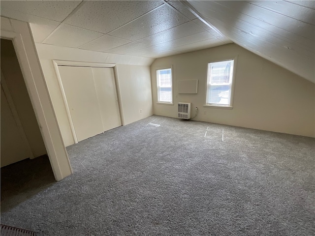 additional living space with vaulted ceiling, heating unit, and carpet