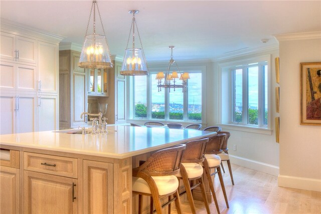 kitchen featuring a kitchen breakfast bar, a notable chandelier, an island with sink, sink, and ornamental molding