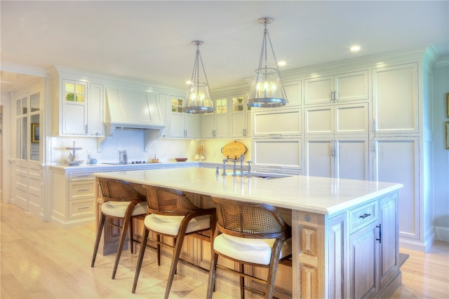 kitchen with light hardwood / wood-style flooring, custom range hood, decorative backsplash, and a kitchen island with sink