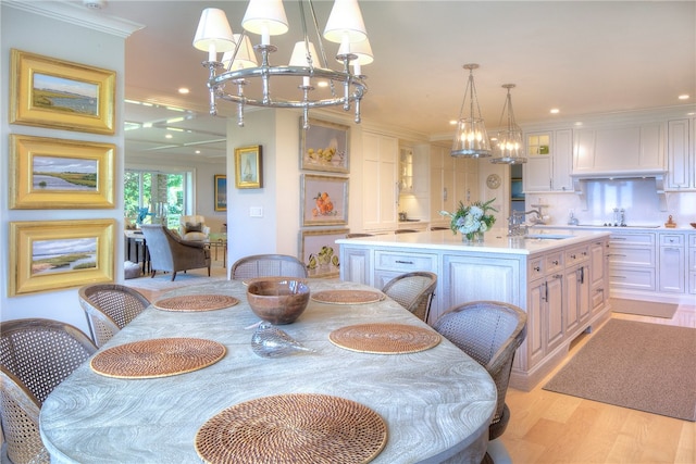 dining space featuring crown molding, sink, a notable chandelier, and light hardwood / wood-style floors