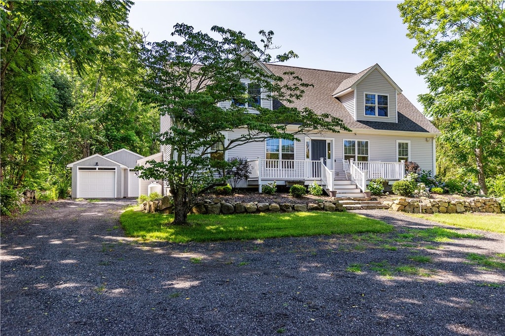 new england style home with a garage, a porch, and an outbuilding