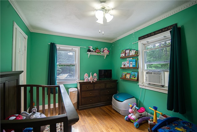 bedroom with crown molding, light hardwood / wood-style flooring, a crib, ceiling fan, and a textured ceiling