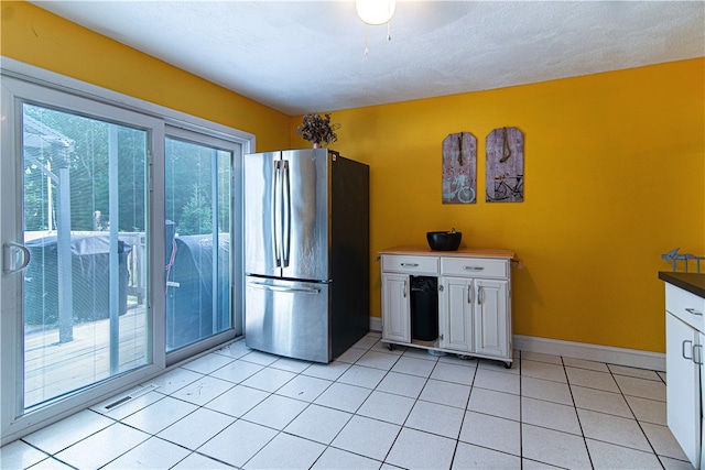 kitchen with white cabinets, stainless steel fridge, and light tile patterned floors