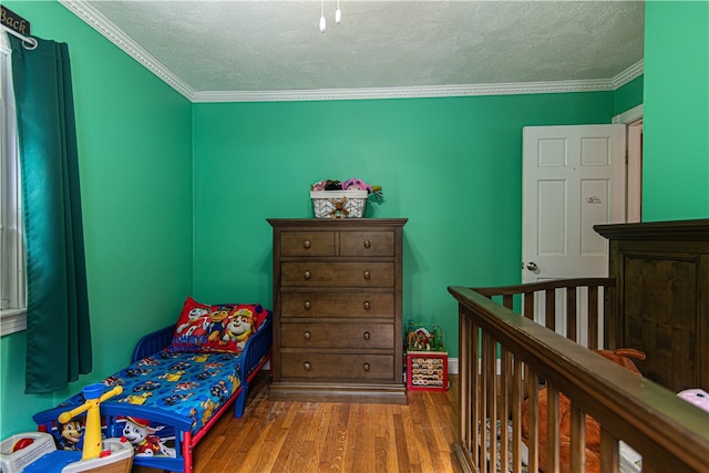 bedroom featuring crown molding, a textured ceiling, wood-type flooring, and a nursery area