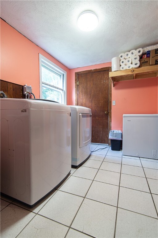 laundry area featuring light tile patterned floors, washing machine and dryer, and a textured ceiling