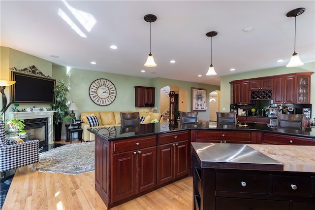 kitchen with light wood-type flooring, a fireplace, a center island, and decorative light fixtures