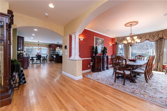 dining room featuring a notable chandelier, light wood-type flooring, ornamental molding, and ornate columns