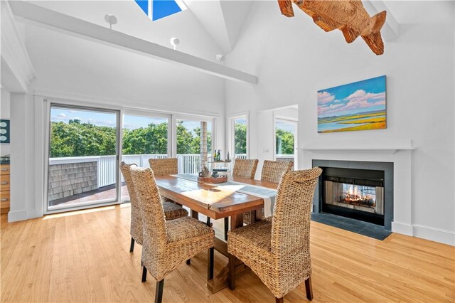 dining room featuring a multi sided fireplace, light hardwood / wood-style floors, a high ceiling, and beam ceiling