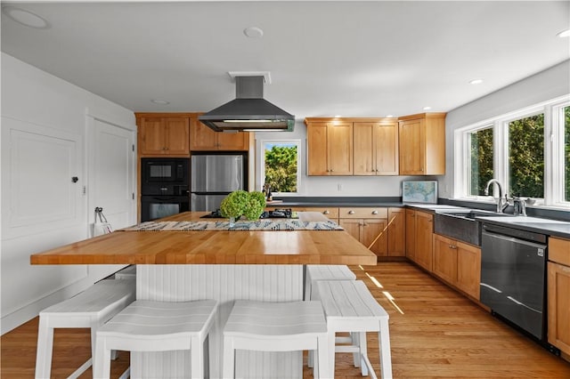 kitchen featuring black appliances, a kitchen island, island exhaust hood, butcher block counters, and light hardwood / wood-style floors