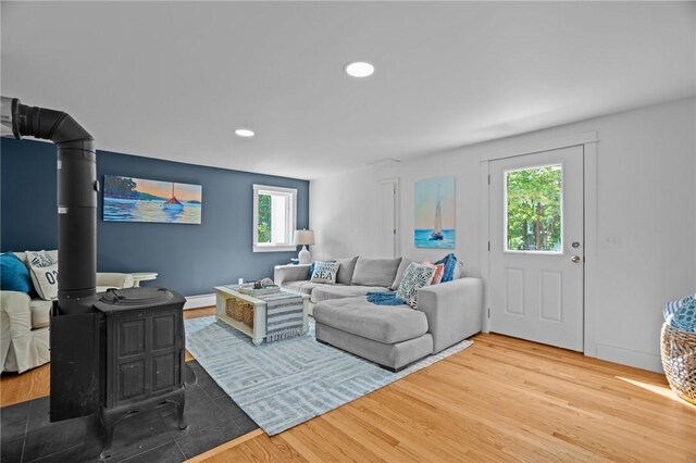 living room featuring a wood stove, hardwood / wood-style floors, a baseboard heating unit, and plenty of natural light