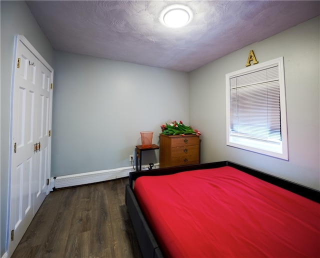 bedroom featuring a closet, baseboard heating, dark wood-type flooring, and a textured ceiling