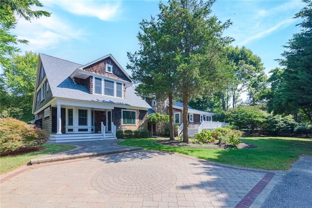 view of front facade with a porch, curved driveway, a shingled roof, and a front yard