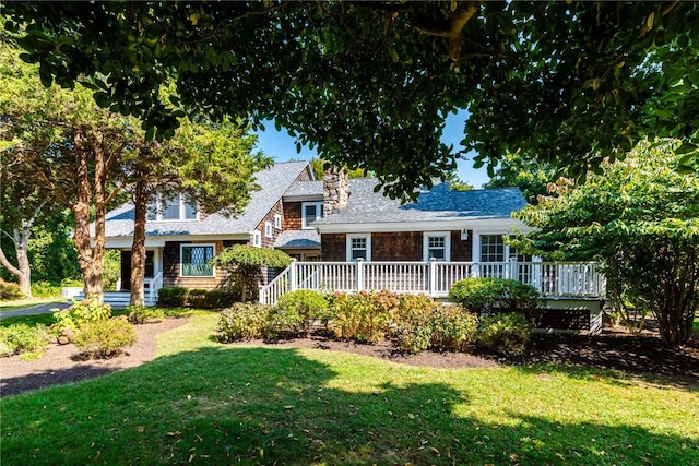 view of front facade featuring roof with shingles, a wooden deck, and a front lawn