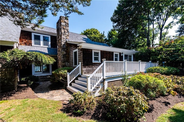 view of front facade featuring a wooden deck, a shingled roof, and a chimney