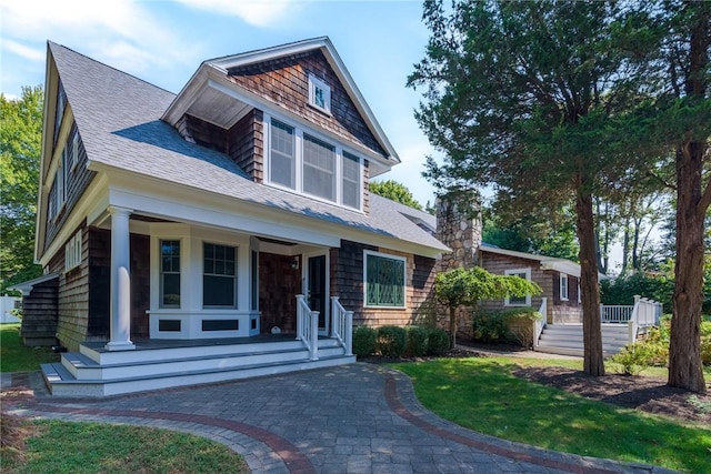 view of front of home with a porch, a shingled roof, and a chimney