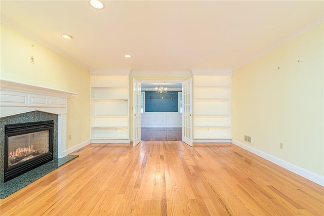 unfurnished living room with crown molding, light wood-style floors, a premium fireplace, a chandelier, and baseboards