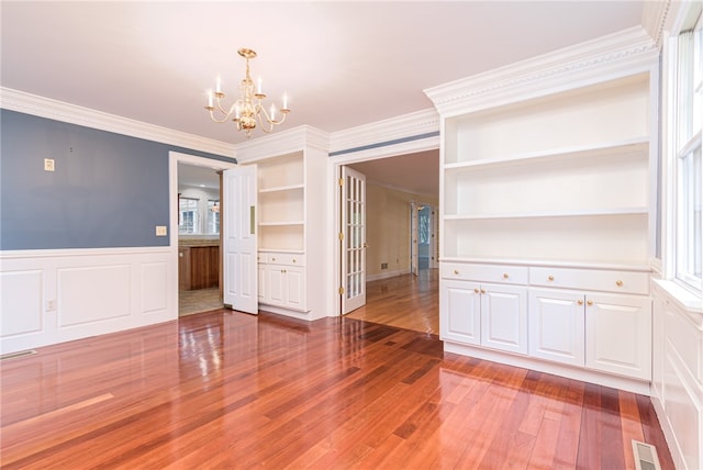 unfurnished dining area with wood-type flooring, a chandelier, built in shelves, a healthy amount of sunlight, and ornamental molding