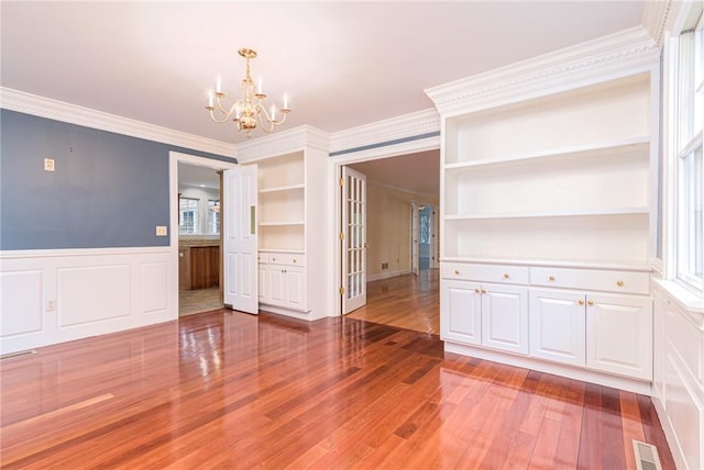 unfurnished dining area featuring crown molding, wainscoting, a decorative wall, wood finished floors, and a chandelier