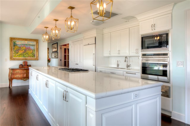 kitchen featuring a kitchen island, sink, built in appliances, white cabinetry, and hanging light fixtures