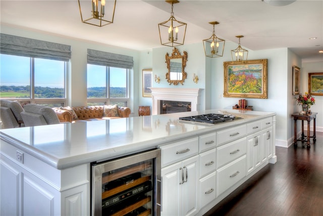 kitchen with stainless steel gas stovetop, hanging light fixtures, a kitchen island, white cabinetry, and beverage cooler