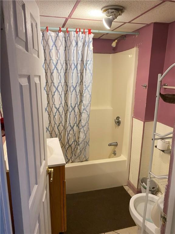 full bathroom featuring toilet, shower / tub combo with curtain, a paneled ceiling, tile patterned flooring, and vanity