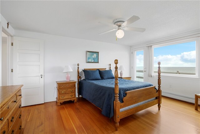 bedroom featuring a water view, ceiling fan, baseboard heating, and hardwood / wood-style flooring