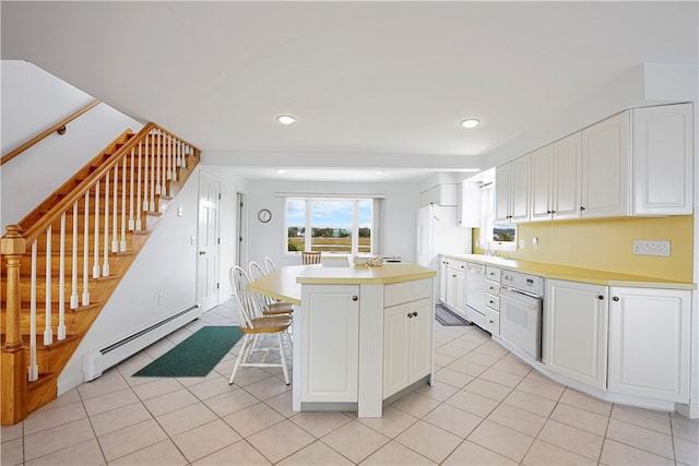 kitchen featuring white cabinetry, white oven, a kitchen island, a kitchen bar, and a baseboard heating unit