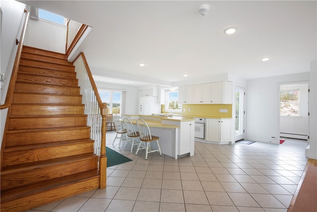 kitchen featuring white cabinetry, light tile patterned flooring, a breakfast bar, white appliances, and baseboard heating